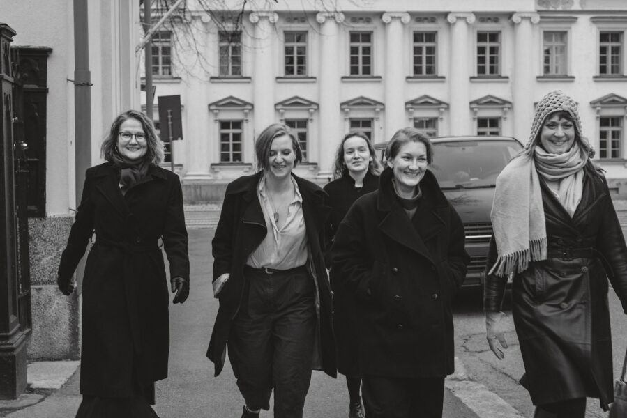 Black and white photo of 5 women walking towards the camera on a street.